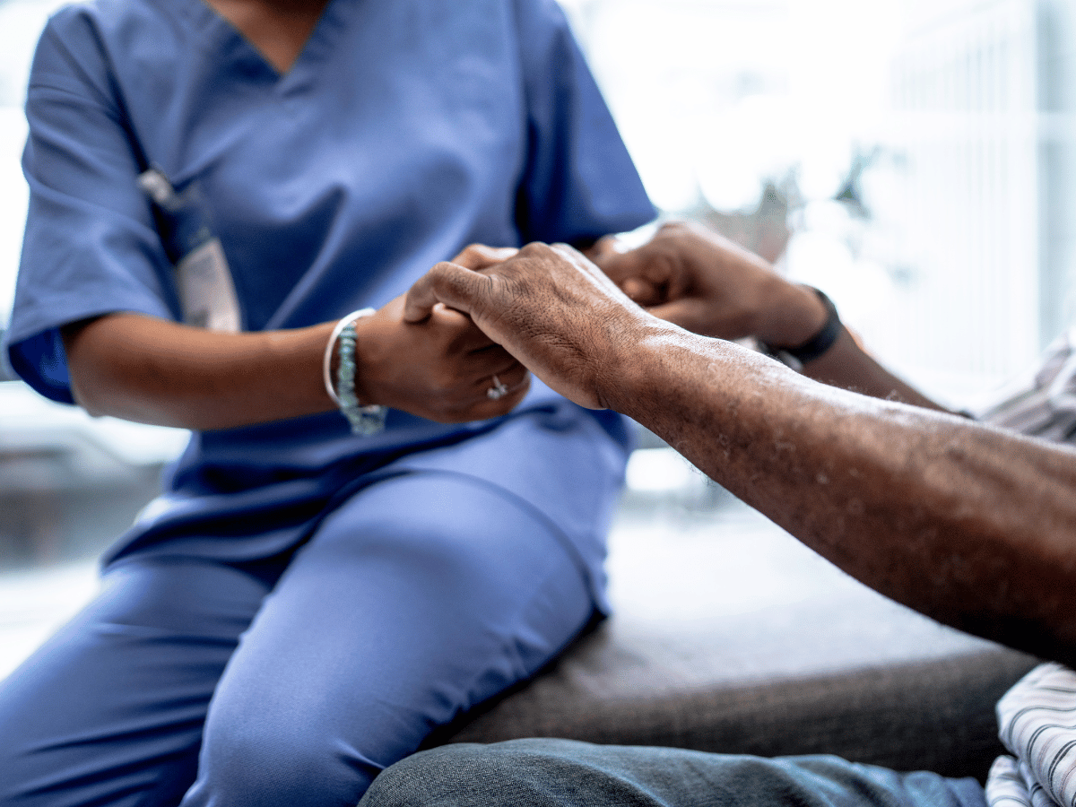 A cropped photo of a female dermatology provider wearing scrubs holding the hand of a patient. Neither faces are in the photo.