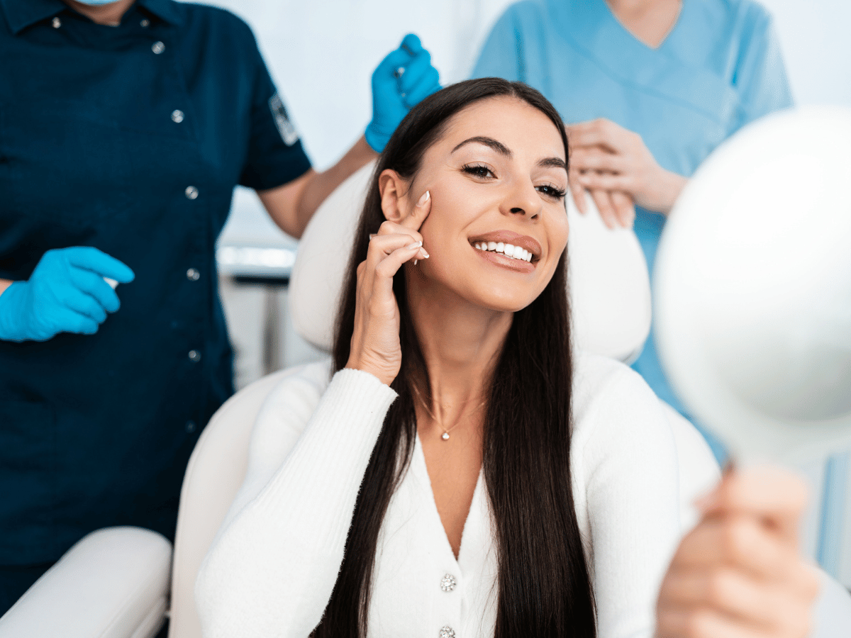 woman in exam room with physicians using handheld mirror to look at face